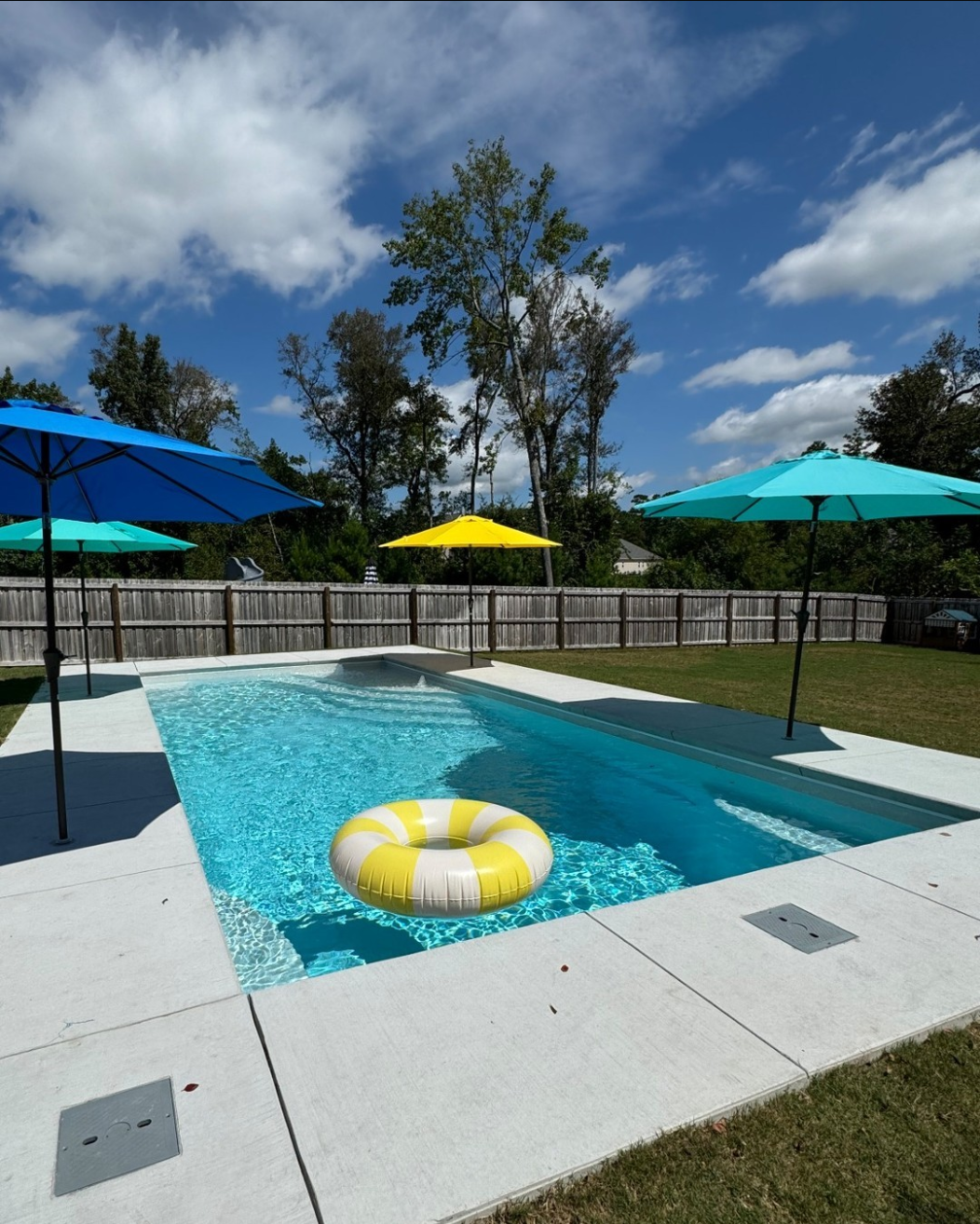 In-ground plaster pool with striped pool float and surrounding multi-colored umbrellas.